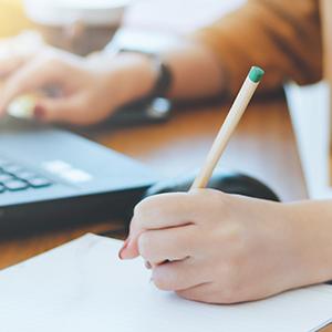 Female hands writing on paper with laptop in background